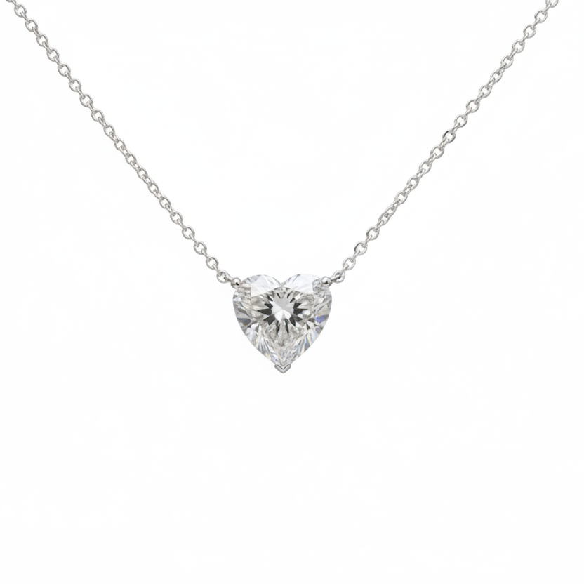 Heart-shaped diamond pendant on a chain held by a hand against a neutral background